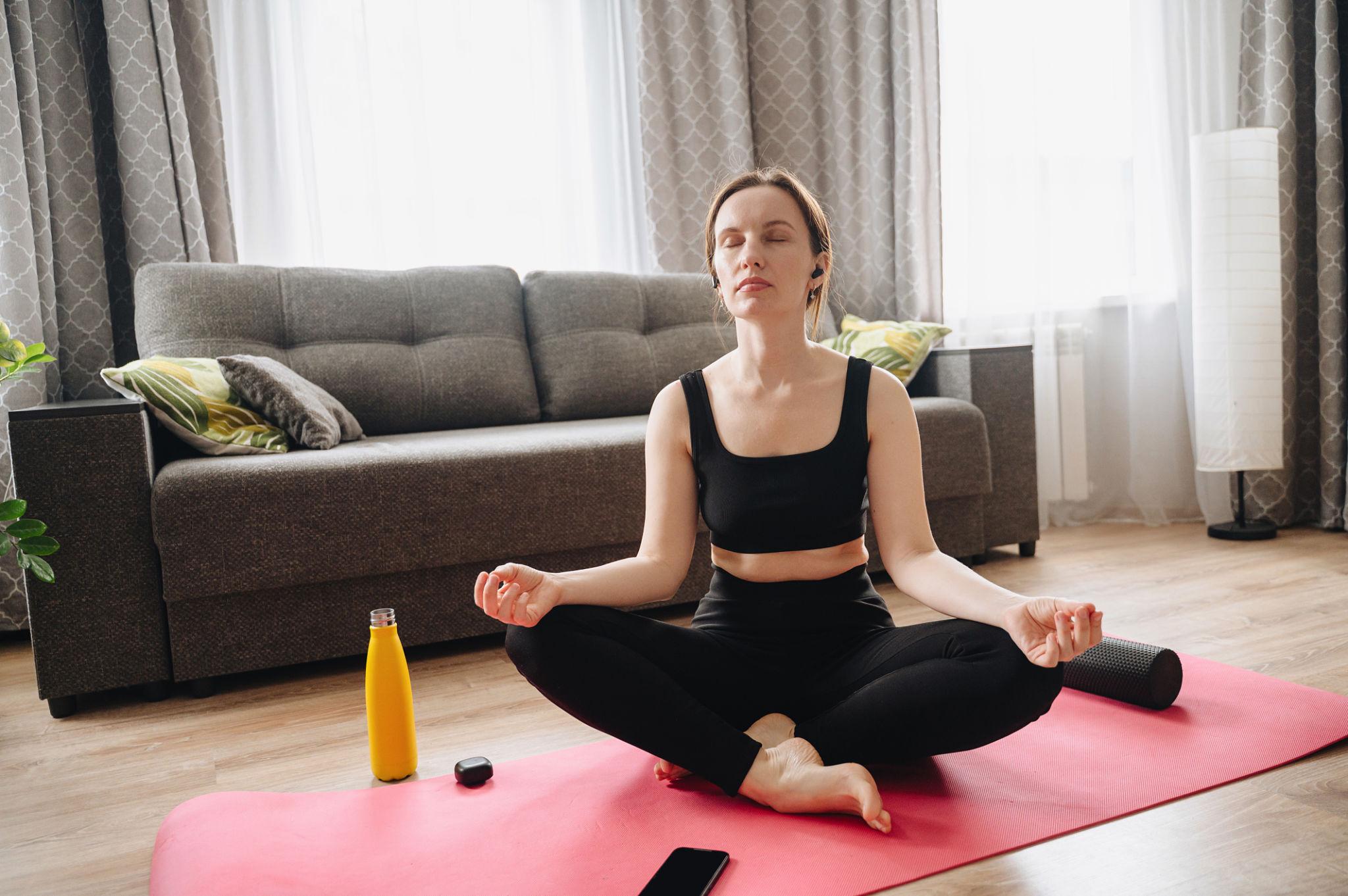 A woman meditating with a smartphone nearby, using a mindfulness or mental health app with a blank mobile screen