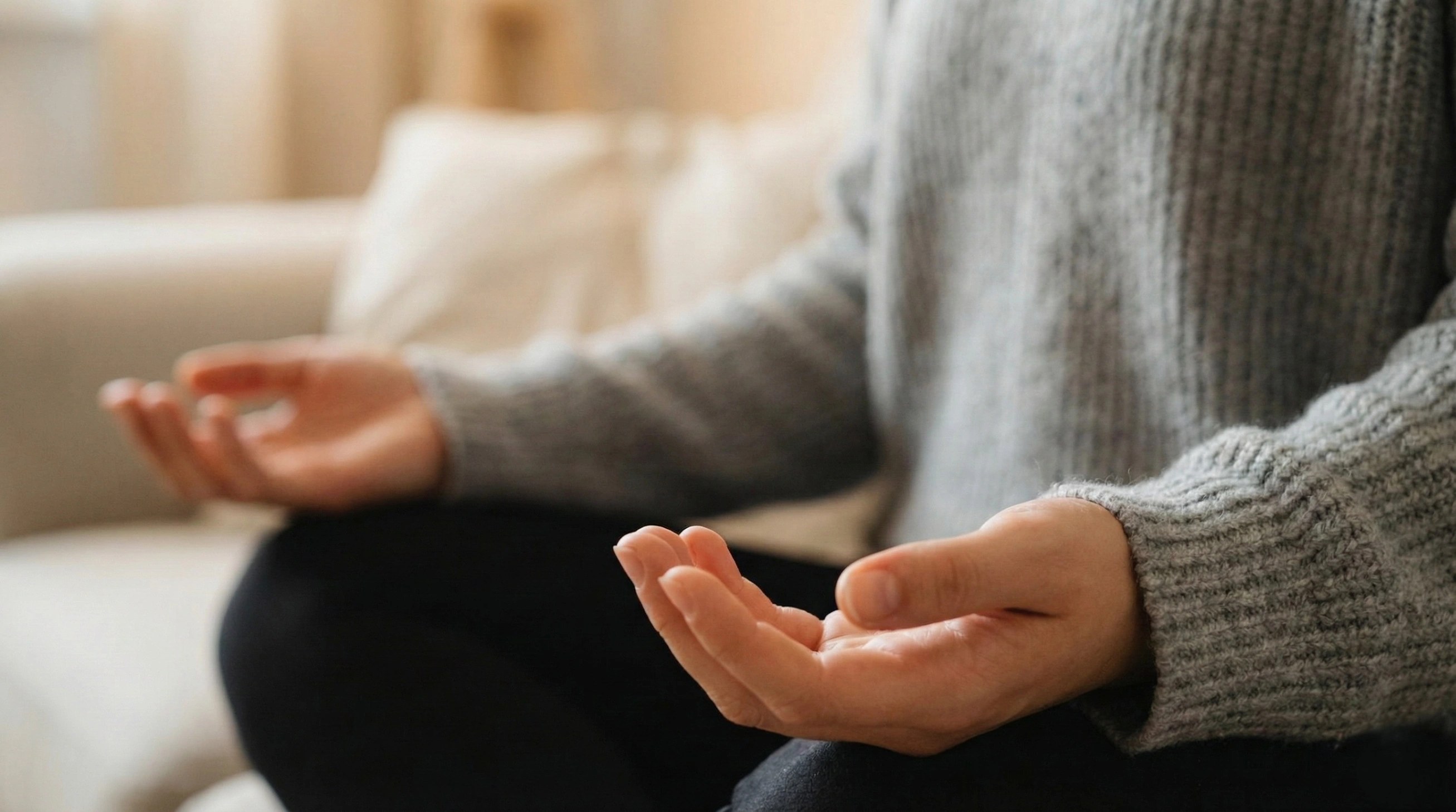 A close-up photograph of a person in a grey sweater sitting comfortably with their hands resting gently, palms up, in their lap during a beginner