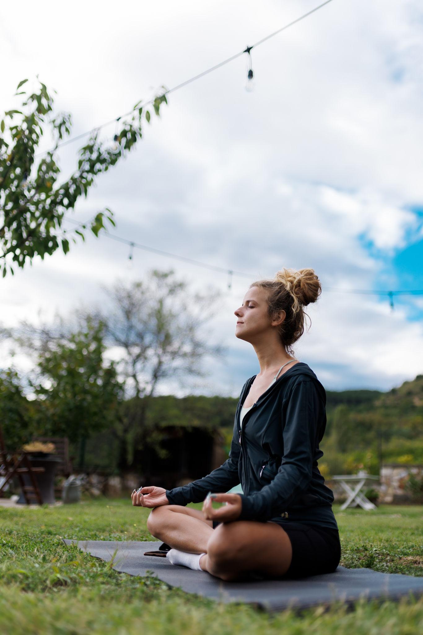 Meditation practice of a woman in nature during a cloudy day with strings of lights in the background