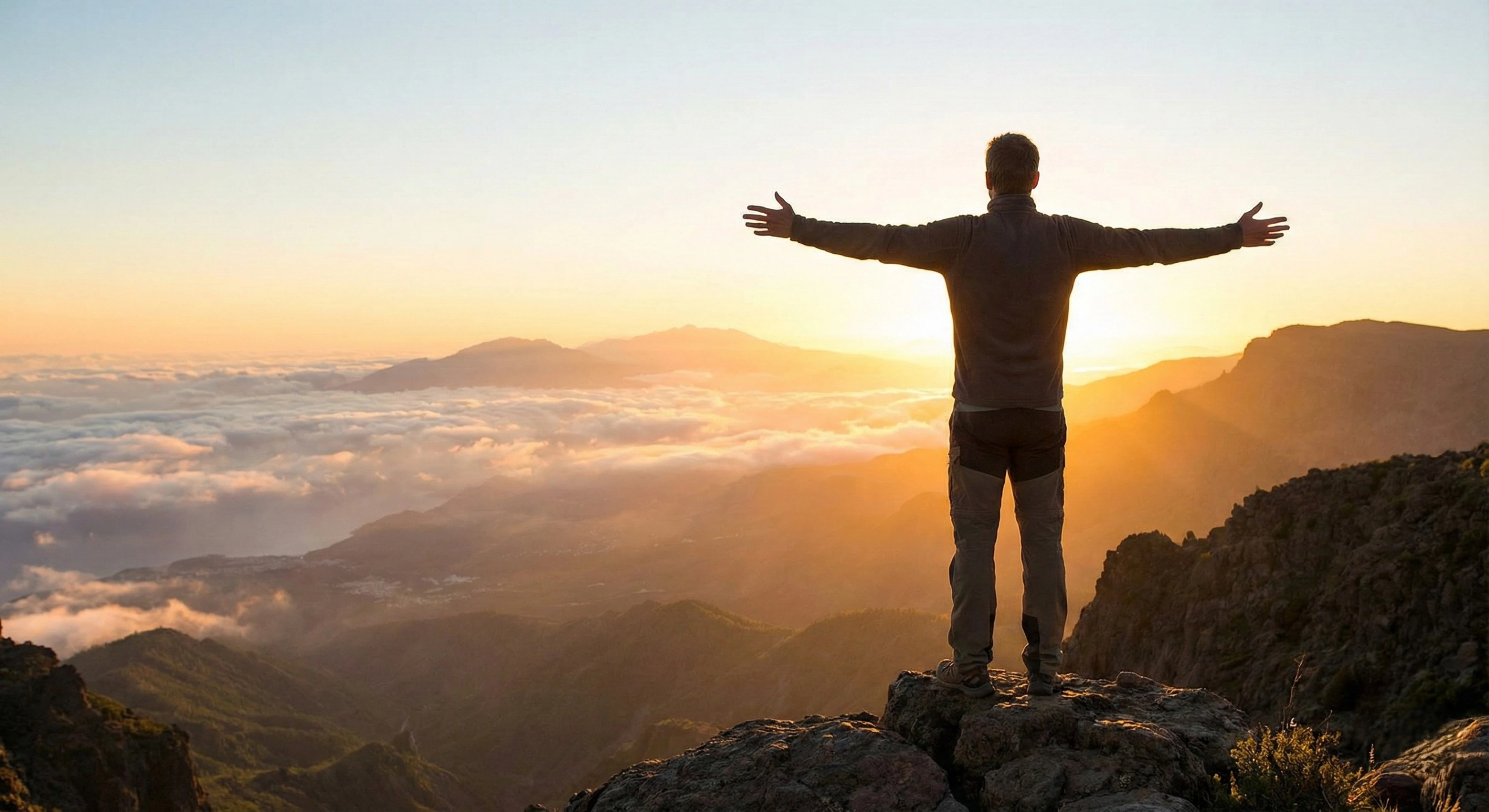 A man stands on a mountain peak at sunrise with his arms outstretched, overlooking a sea of clouds, symbolizing the spiritual freedom and profound connection with nature that meditation can foster.