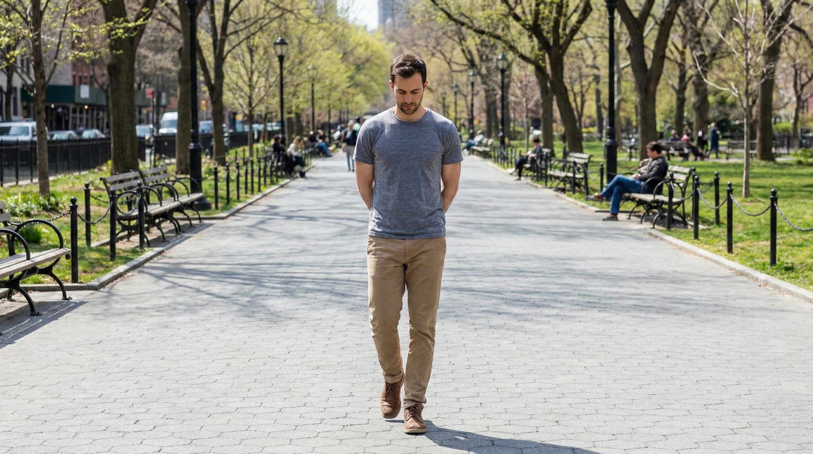 Man walking slowly and deliberately down a paved path in a sunny urban park, performing a walking meditation.