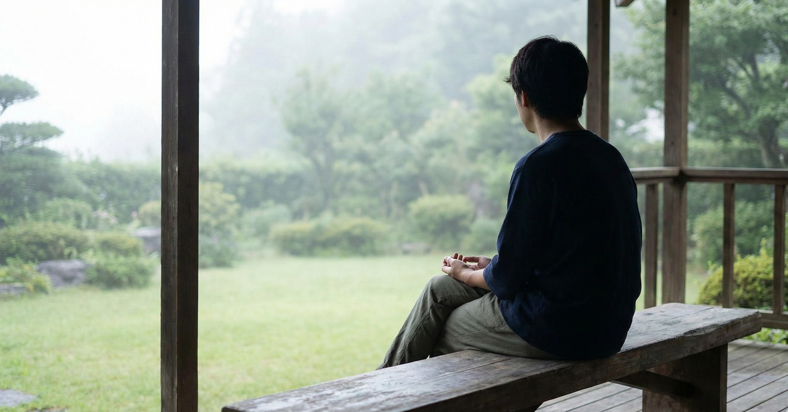 A person sitting on a porch bench, looking out at a misty garden, practicing the art of doing nothing.