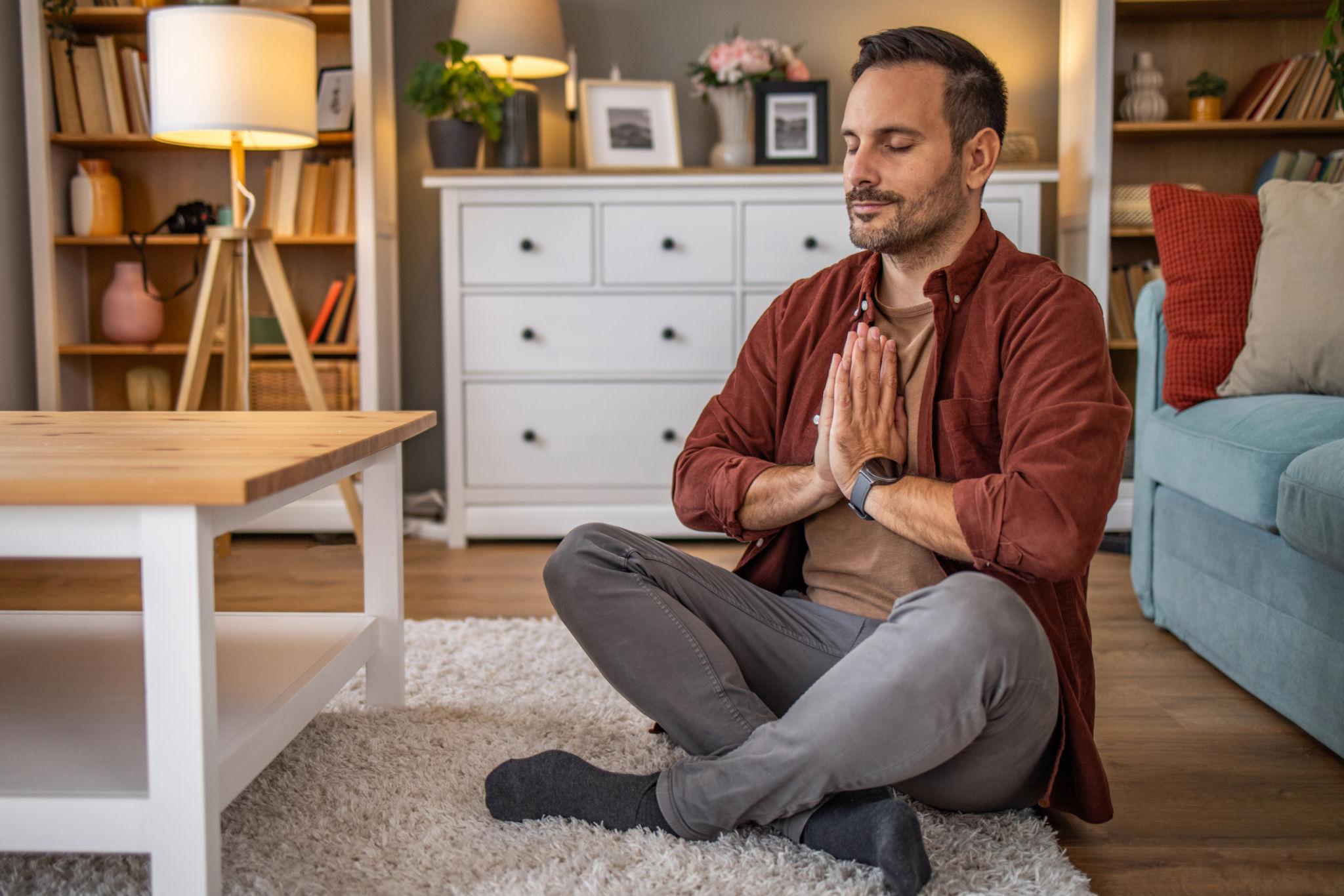 Middle aged man sitting on floor practicing guided meditation at home, relaxing body and mind concept