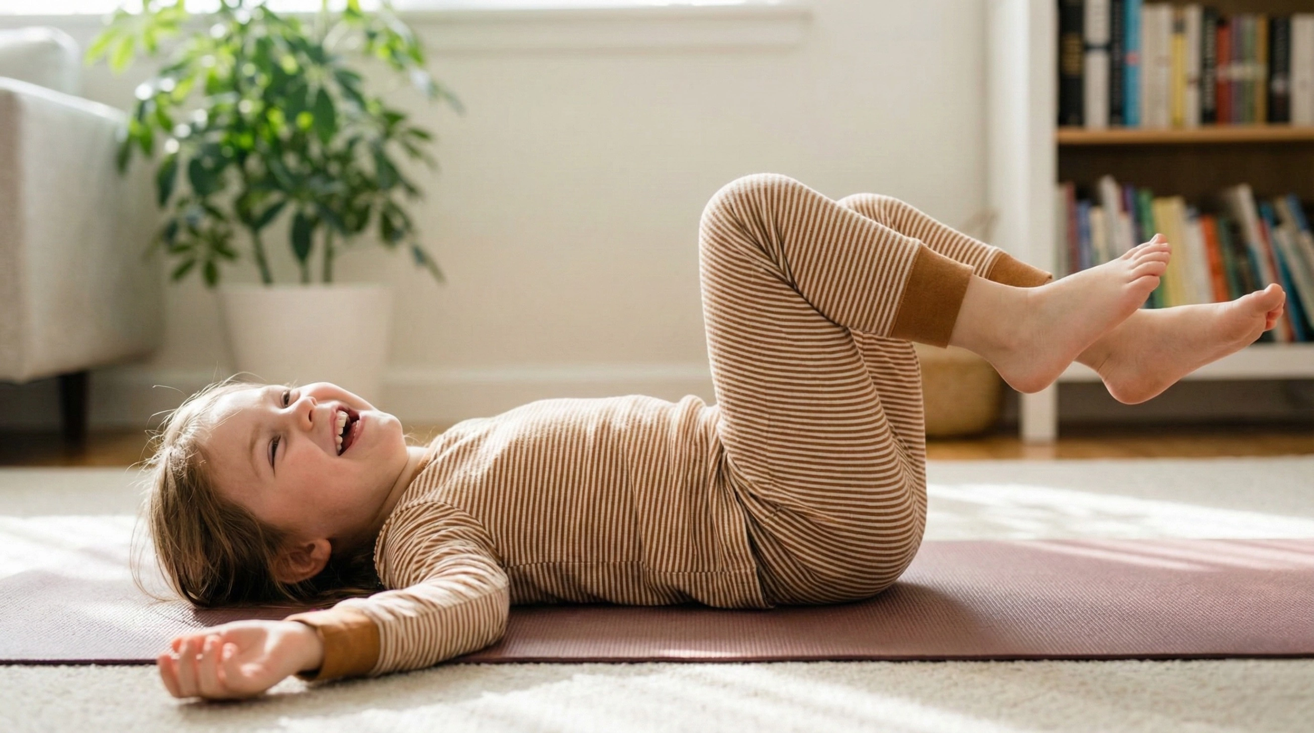 A happy young child lying on their back on a yoga mat, laughing and wiggling, demonstrating the